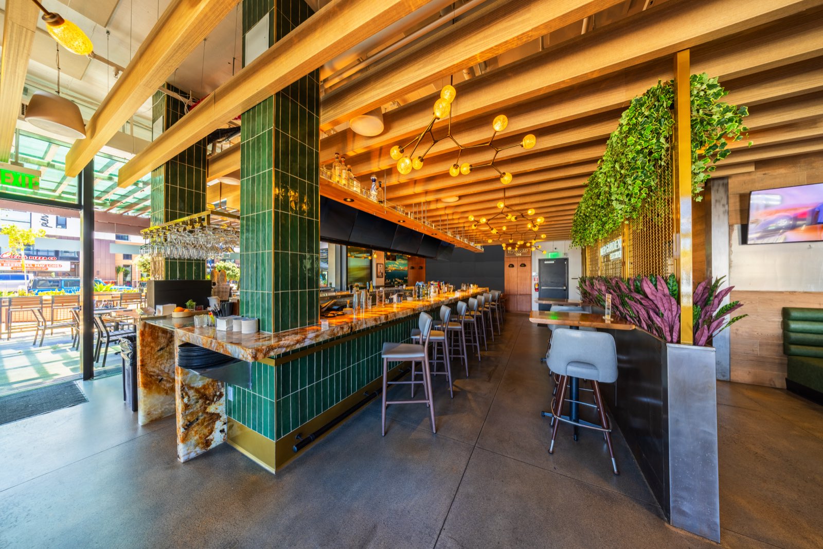 Green-tiled bar with high-top seating and hanging greenery
